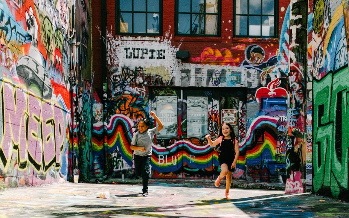 A wide alley way with bright graffiti and two children smiling and jumping