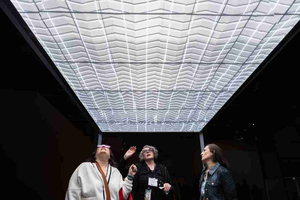 Three people look up in wonderment in a museum installation with a lighted ceiling