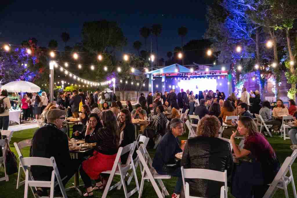 A photo of a scenic museum garden space with dozens of people enjoying a meal together