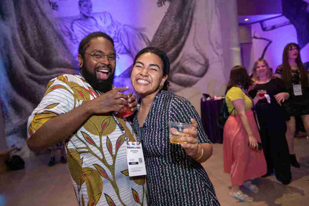 Two people raise their glasses with big smiles at the AAM party