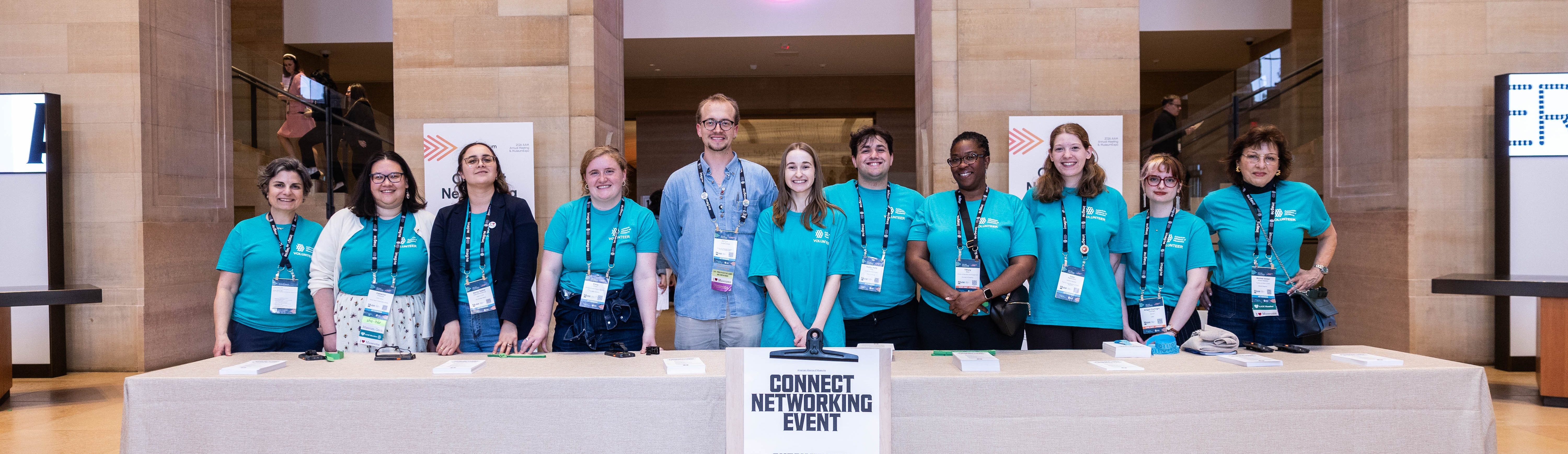 A group of volunteers in teal t shirts smiling for a photo